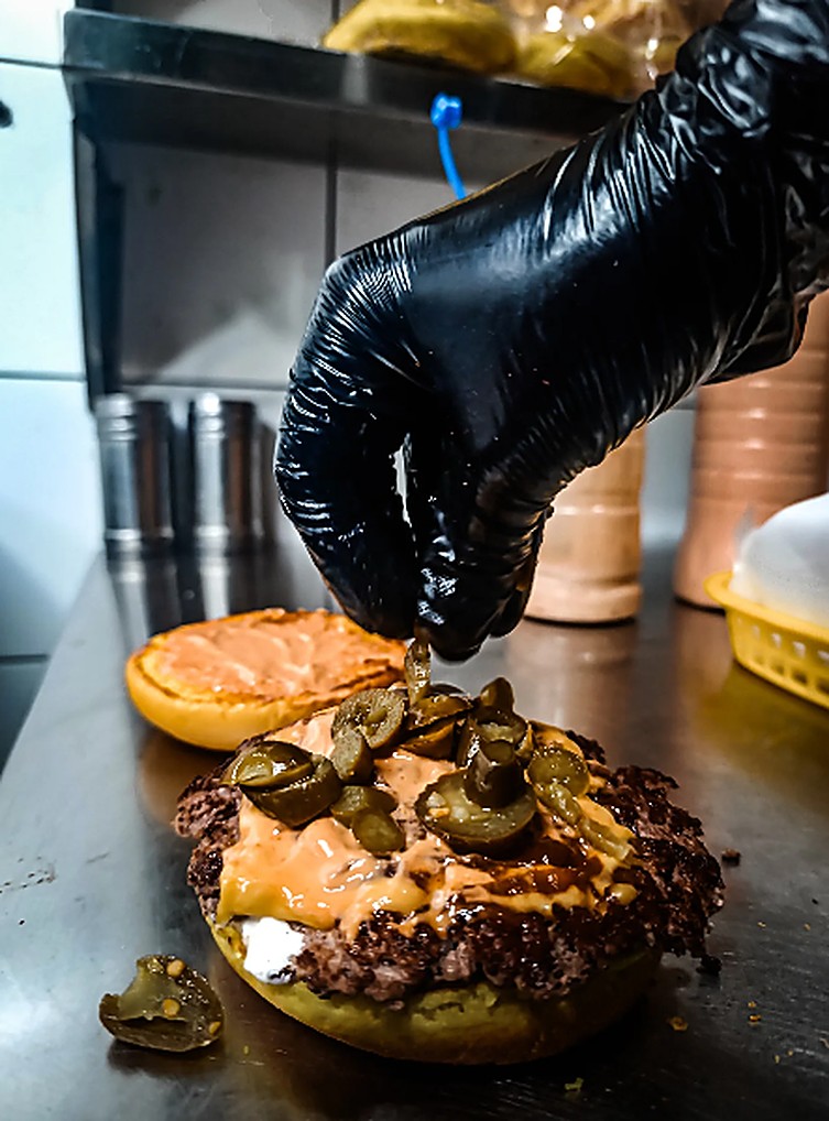Jalapeños being placed on a sauced smash patty at Lorenzo